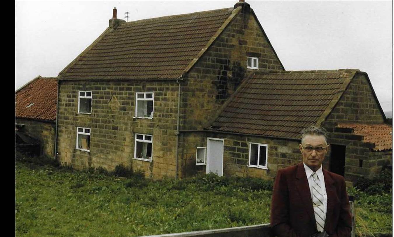 An old brick building with grass in front of a house

Description automatically generated