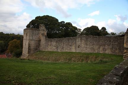 A stone wall with a stone wall in the middle with Pickering Castle in the background

Description automatically generated