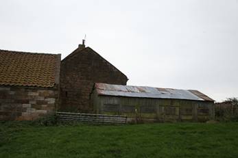 A stone building with a barn in the background

Description automatically generated
