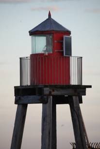 A red lighthouse on a pier

Description automatically generated
