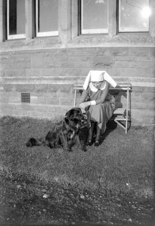 A person wearing a nun's hat and sitting on a bench with a dog

Description automatically generated