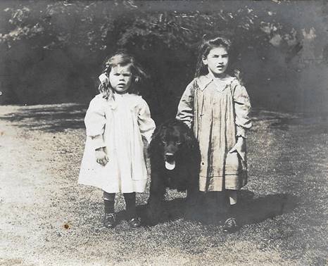 A couple of girls standing next to a dog

Description automatically generated