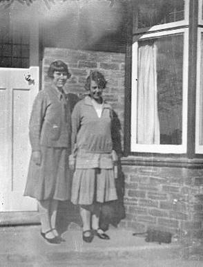 A couple of women standing outside a house

Description automatically generated
