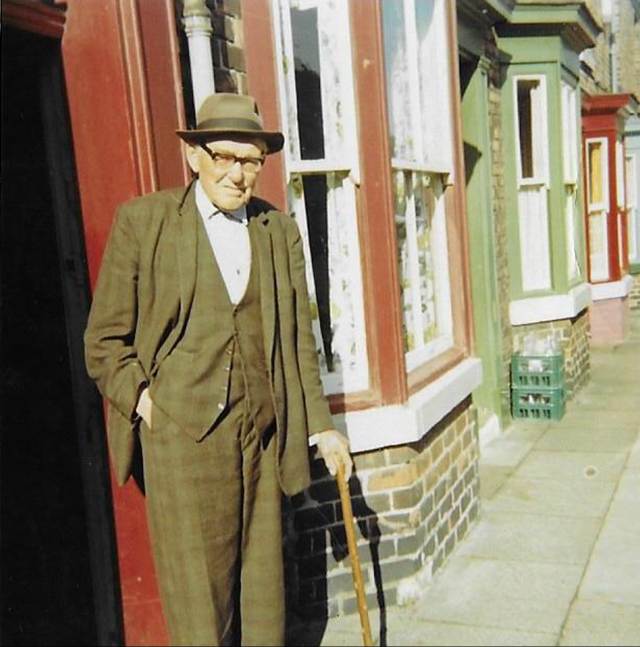A person in a suit and hat standing outside a building
Description automatically generated