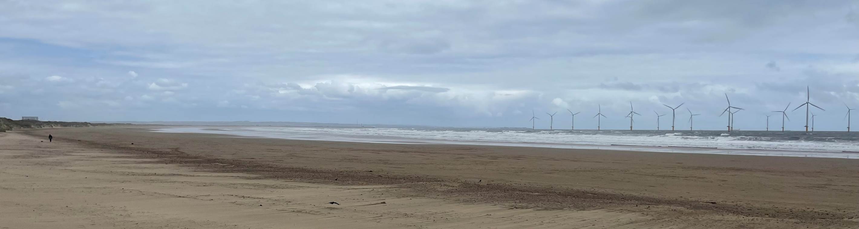 A sandy beach with waves in the background with Camber Sands in the background
Description automatically generated
