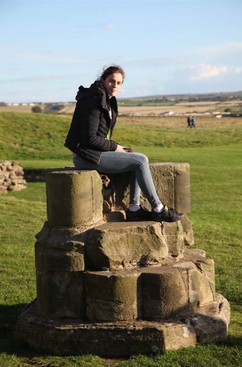 A person sitting on a stone pillar
Description automatically generated
